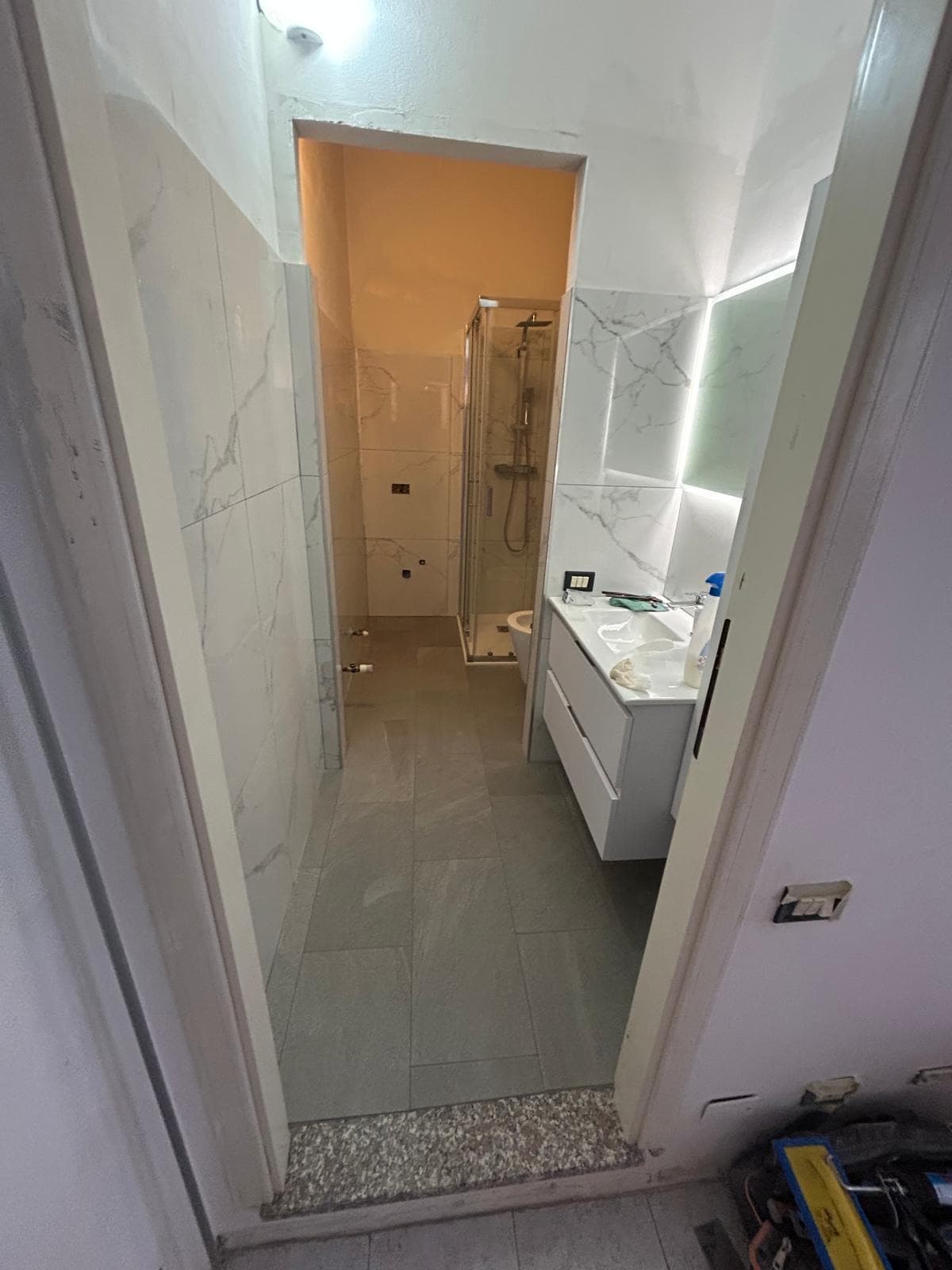 Bagno completamente ristrutturato con pareti effetto marmo, mobile sospeso e specchio LED