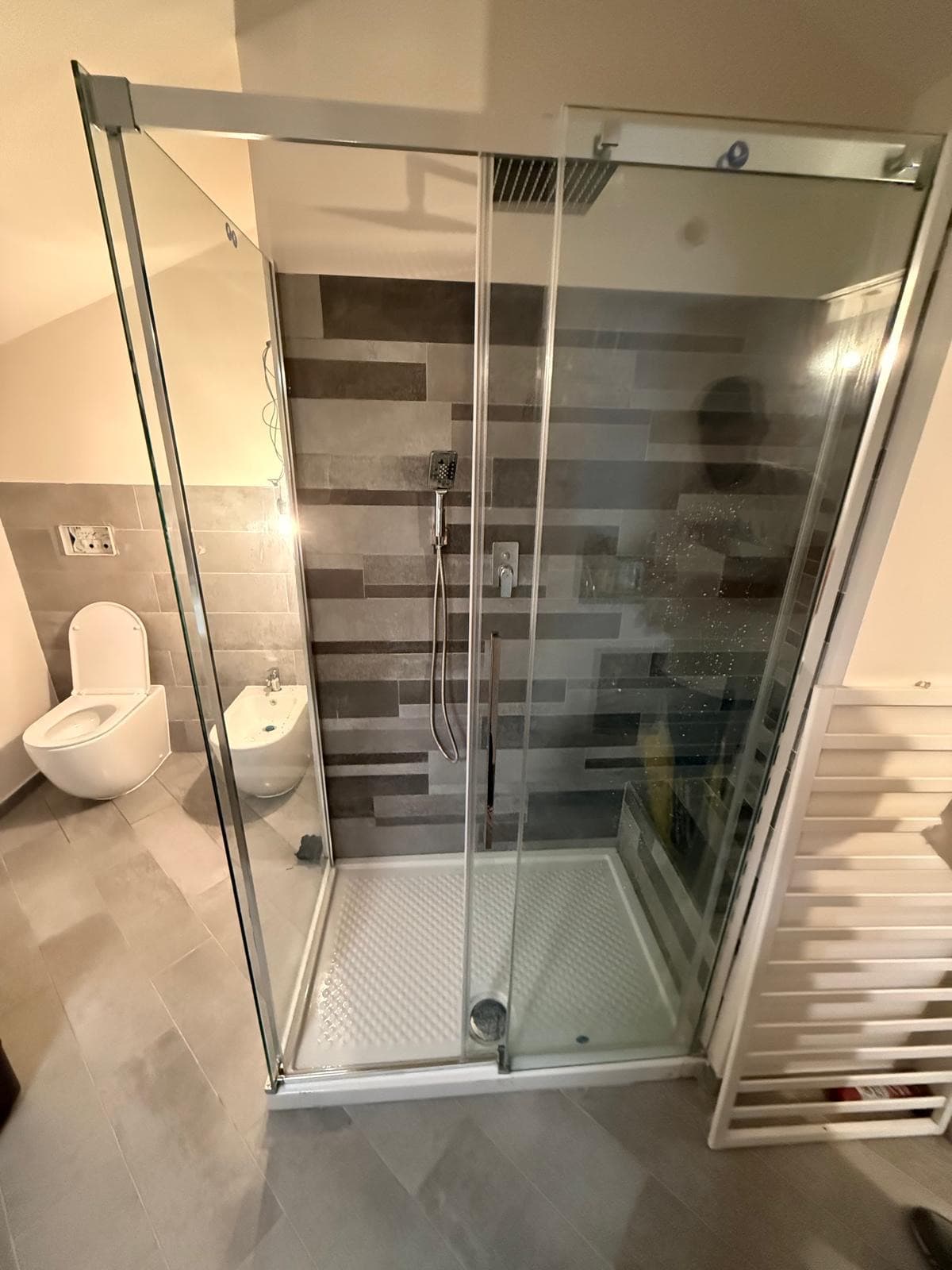 Box doccia scorrevole in un bagno mansardato con rivestimento grigio