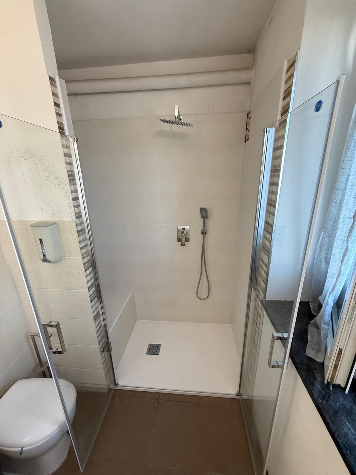 Doccia con porte a battente aperte, piatto bianco e soffione a soffitto